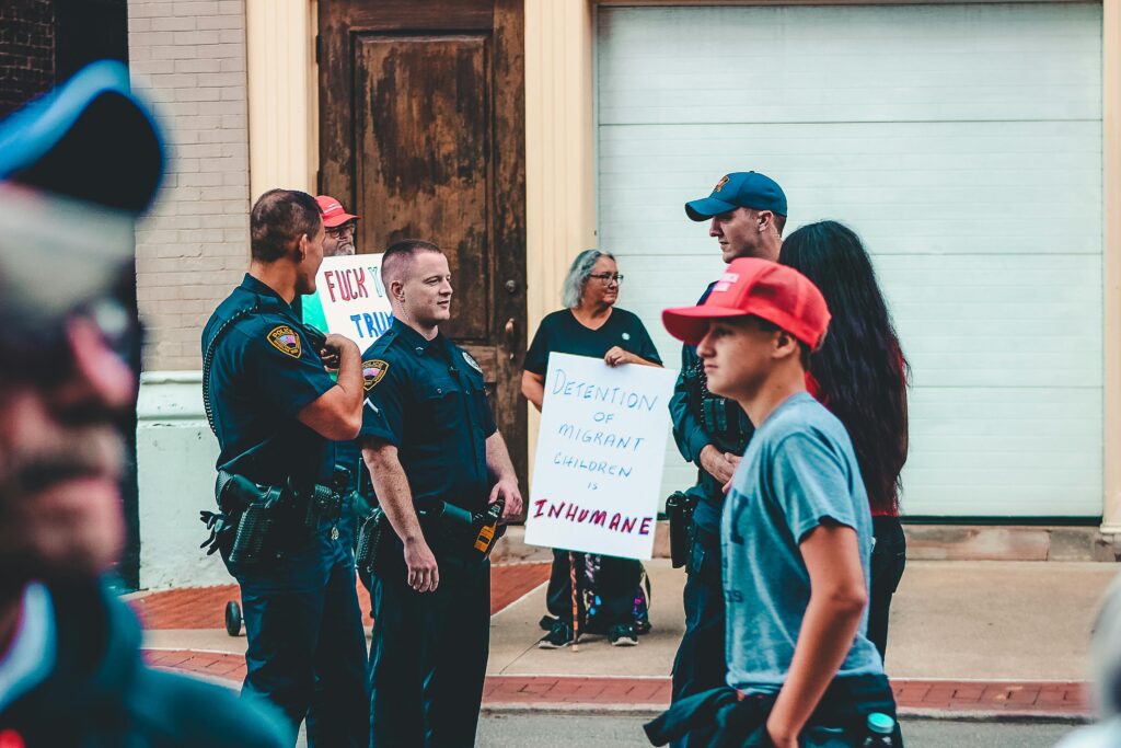 Protestors against deportation holding signs. Police presence keeping the peace and young man in a red hat.